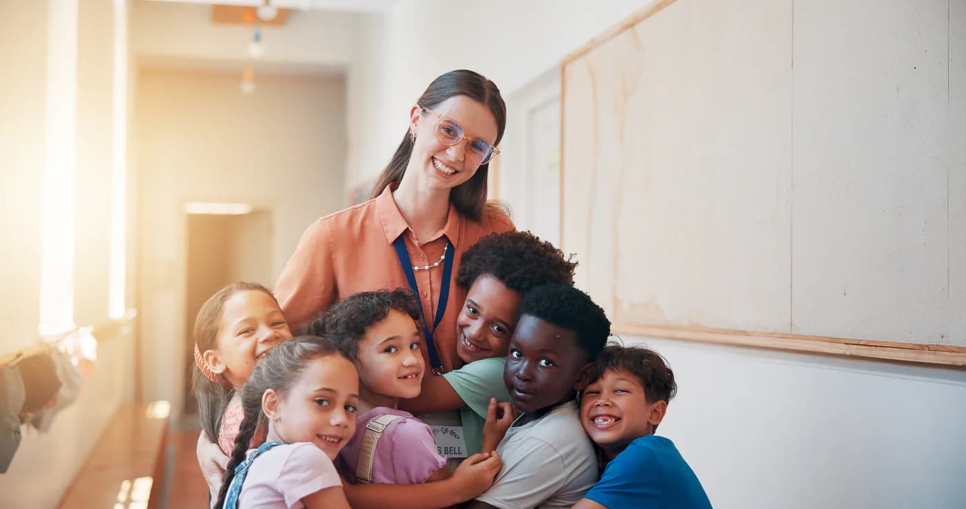 A teacher and six children smile together in their classroom.