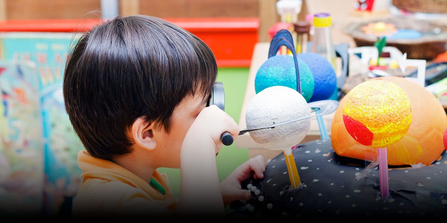A young child looks through a toy telescope beside a model of the solar system.