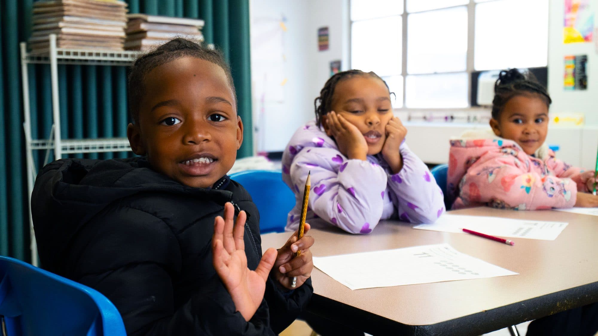 Three young students seated together at a classroom table.